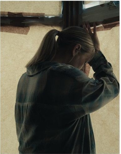 Maddy beside a window papered over with tape, blocking the daylight